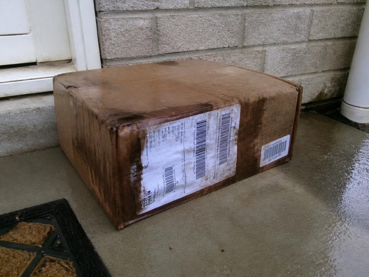 Rain-soaked cardboard parcel with dark water stains on a porch