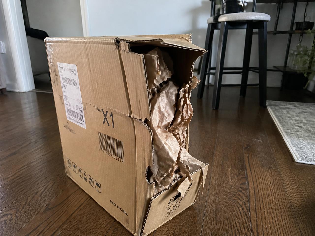 Shipping box torn open along the corner with packing paper spilling out